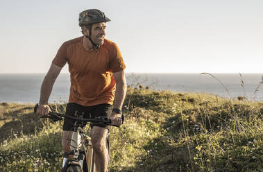 Male athlete cycling while looking away at sunset - UUF23750