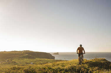 Männlicher Sportler fährt Fahrrad in grüner Landschaft am Meer - UUF23752
