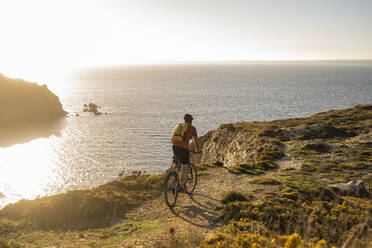 Älterer Sportler mit Rucksack Radfahren auf Klippe am Meer - UUF23753