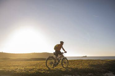 Männlicher Sportler fährt Mountainbike auf einer Wiese - UUF23761