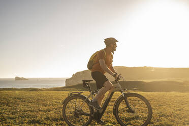 Männlicher Sportler auf einem elektrischen Mountainbike auf einer Wiese - UUF23762