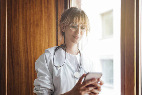 Ärztin benutzt Mobiltelefon am Fenster in der Klinik - EGHF00053