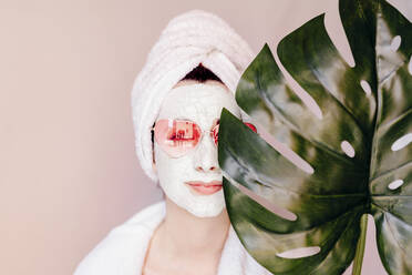 Junge Frau mit Schönheitsmaske, die das Auge mit einem Monstera-Blatt bedeckt - EGHF00059