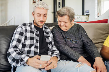 Junger Mann teilt Mobiltelefon mit Großmutter zu Hause - MEUF03181