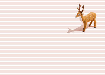 Studio shot of reindeer figurine standing against pink striped background - FLMF00530