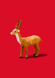 Studio shot of reindeer figurine standing against vibrant red background - FLMF00531