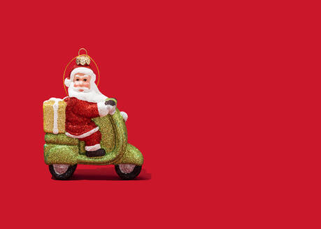 Christmas ornament of Santa Claus riding motor scooter against vibrant red background - FLMF00534