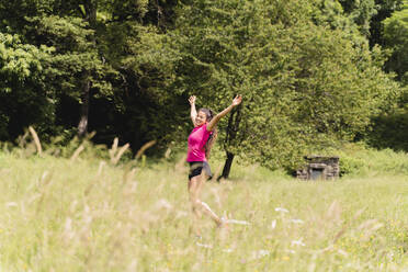 Smiling woman with arms raised standing in meadow - FMOF01451