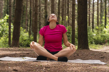 Young woman doing relaxation exercise while sitting in forest - FMOF01453