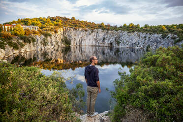 Man standing on rock formation while looking at Lake Dragon's Eye, Rogoznica, Croatia - MAMF01898