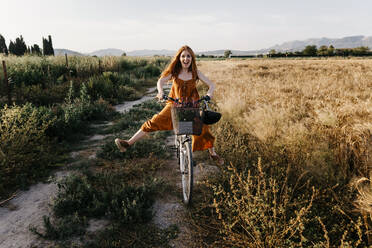 Carefree woman riding bicycle in agricultural field - TCEF01965