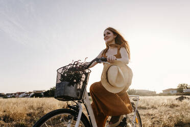 Rothaarige Frau fährt bei Sonnenuntergang Fahrrad in einem Feld - TCEF01968