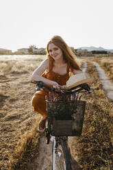 Beautiful woman sitting on bicycle in field - TCEF01969