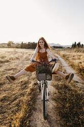 Carefree redhead woman riding bicycle in field - TCEF01970