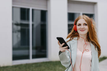 Beautiful businesswoman holding mobile phone while listening music through headphones - TCEF01985