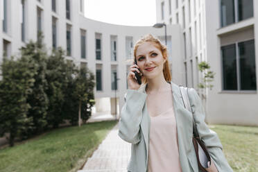 Weibliche Fachkraft, die wegschaut, während sie im Büropark mit einem Mobiltelefon spricht - TCEF01988