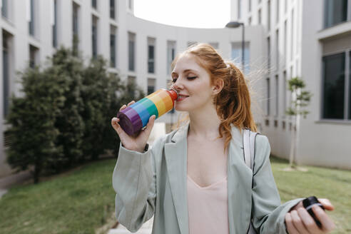 Businesswoman drinking water from rainbow bottle in office park - TCEF01990