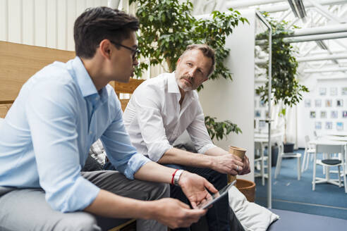 Geschäftsmann hört einem Kollegen mit digitalem Tablet im Büro zu - DIGF15936