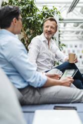 Smiling businessman with coffee cup sitting by colleague at office - DIGF15939