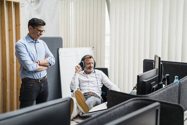 Lächelnder Geschäftsmann mit verschränkten Armen, der neben einem Kollegen im Büro steht - DIGF15951