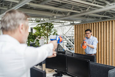 Male colleague holding toy gun while playing in office - DIGF15956