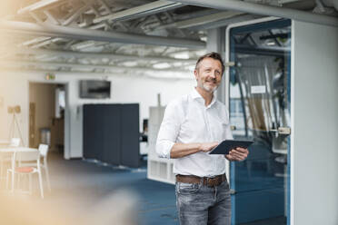 Männlicher Berufstätiger, der ein digitales Tablet hält, während er im Büro steht - DIGF15961