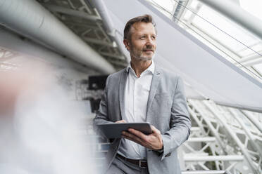 Thoughtful male professional holding digital tablet while standing in office - DIGF15980