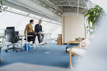 Geschäftsleute diskutieren auf dem Schreibtisch sitzend im Büro - DIGF15995