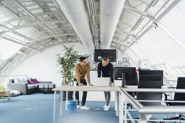 Businessmen with laptop discussing while leaning on desk - DIGF16000