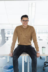 Male professional smiling while sitting on desk in office - DIGF16008
