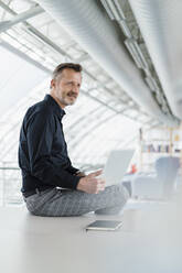 Thoughtful businessman sitting with laptop on desk in office - DIGF16013