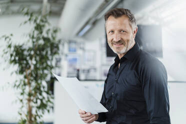 Lächelnder Geschäftsmann hält Papier im Büro - DIGF16019