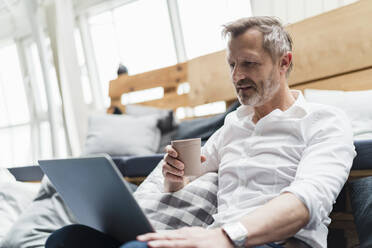 Männlicher Berufstätiger, der einen Einwegbecher hält und einen Laptop im Büro benutzt - DIGF16029