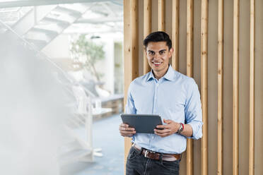 Smiling businessman with digital tablet standing in office - DIGF16030