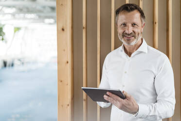 Businessman holding digital tablet while standing in front of wall - DIGF16036