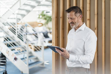 Male professional using digital tablet while standing in office - DIGF16037