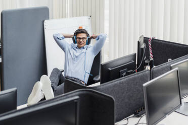 Smiling businessman with hands behind head sitting by desk - DIGF16042