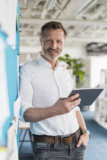 Reifer Geschäftsmann, der ein digitales Tablet hält, während er im Büro steht - DIGF16048