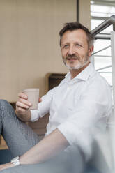 Businessman holding disposable cup while sitting in office - DIGF16055