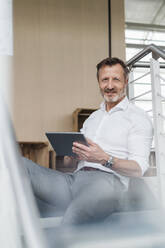 Männlicher Fachmann, der ein digitales Tablet hält, während er auf einer Treppe im Büro sitzt - DIGF16056