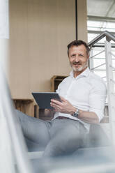 Male professional holding digital tablet while sitting on steps in office - DIGF16056