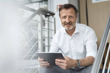 Male professional holding digital tablet while sitting in office - DIGF16057