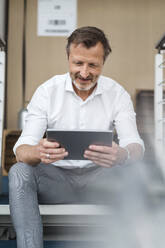 Männlicher Berufstätiger, der ein digitales Tablet benutzt, während er auf einer Treppe sitzt - DIGF16058