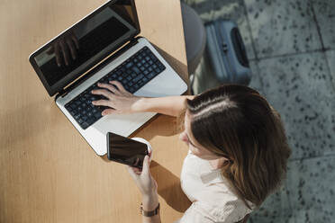 Young female professional sitting with laptop using mobile phone in cafe - EBBF04102