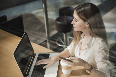 Weibliche Fachkraft mit Laptop am Tisch in einem Café sitzend - EBBF04104