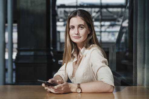 Junge Frau sitzt mit Smartphone in einem Cafe - EBBF04109