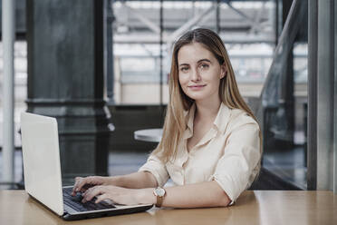 Beautiful young businesswoman sitting with laptop in cafe - EBBF04112