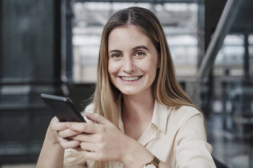 Lächelnde junge schöne Frau sitzt mit Handy im Café - EBBF04116