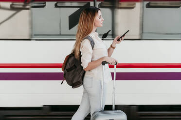 Junge Frau mit Rucksack und Smartphone auf dem Bahnhof - EBBF04122