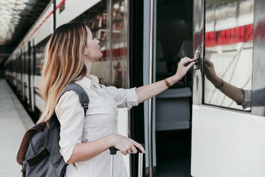 Junger weiblicher Fahrgast drückt Knopf im Zug am Bahnhof - EBBF04124
